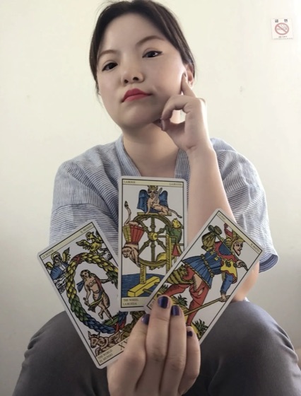 Simone holding a fanned spread of three tarot cards: The World, The Wheel, and The Chariot